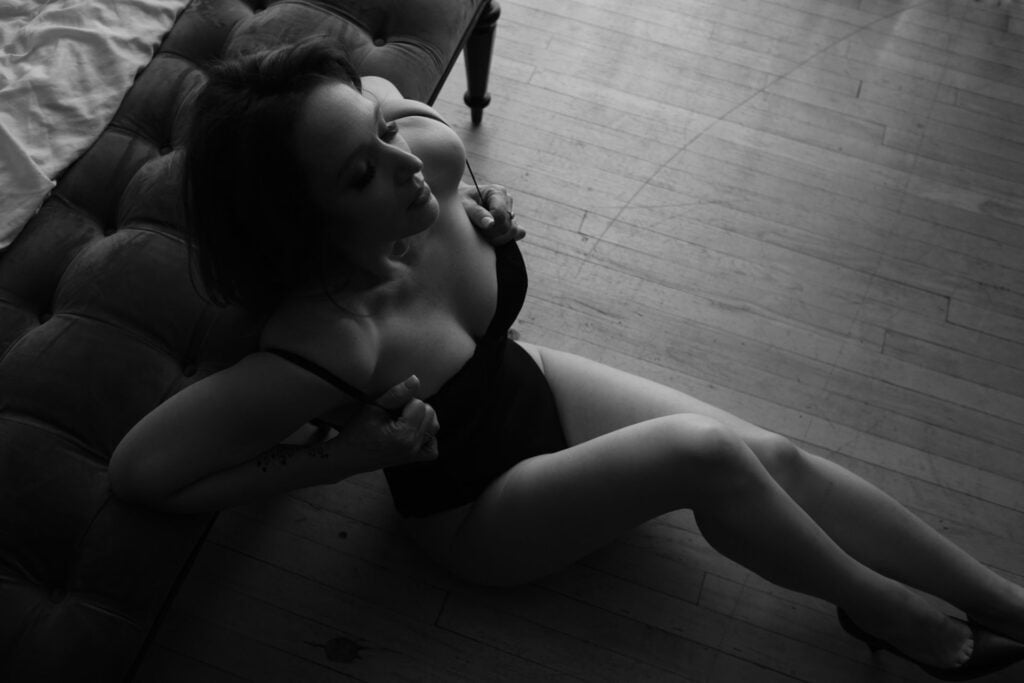B&W boudoir woman sitting on the ground playing with bra straps