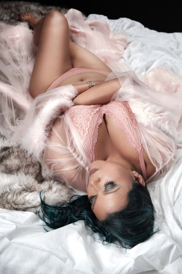 black haired woman lying down on bed in pink lingerie and robe