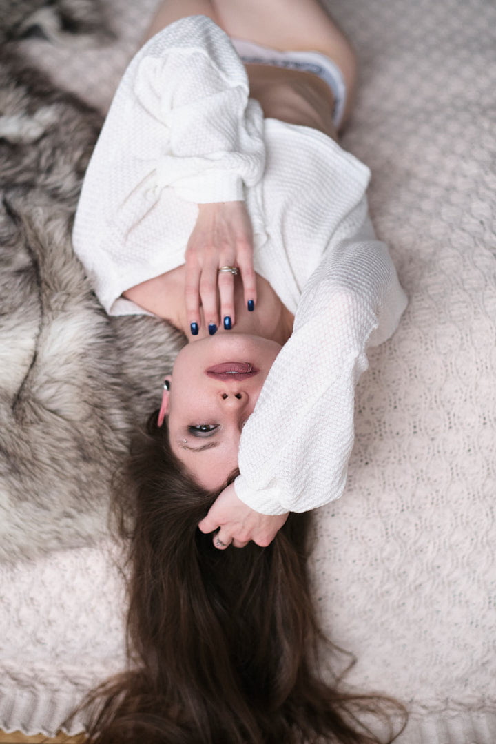 woman lying down on bed in sheer white sweater and underwear sensual suggestive boudoir session in toronto studio