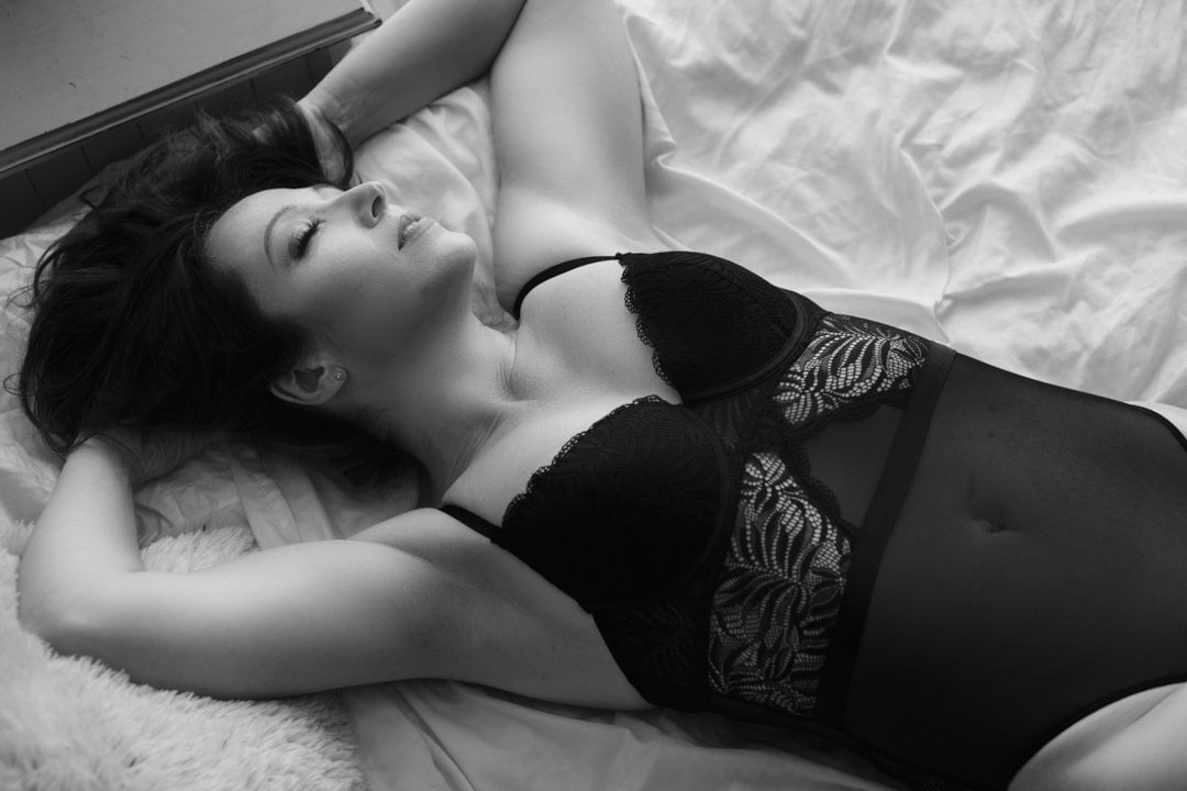 B&W photo of woman lying on bed in black lingerie bodysuit