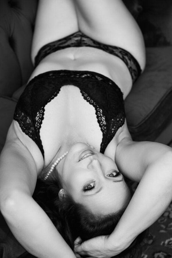 woman lying on couch in two piece black lacy lingerie set and pearls